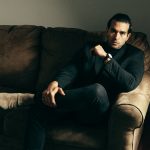 Full body adult serious man in posh suit sitting confidently on sofa and looking at camera