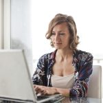 A woman typing on a laptop in a bright, modern home office setting.